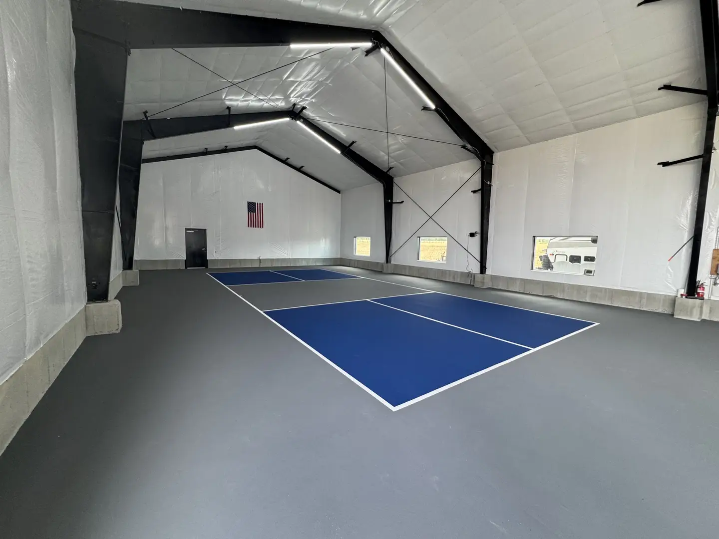 Indoor pickleball court with blue and gray surfaces.