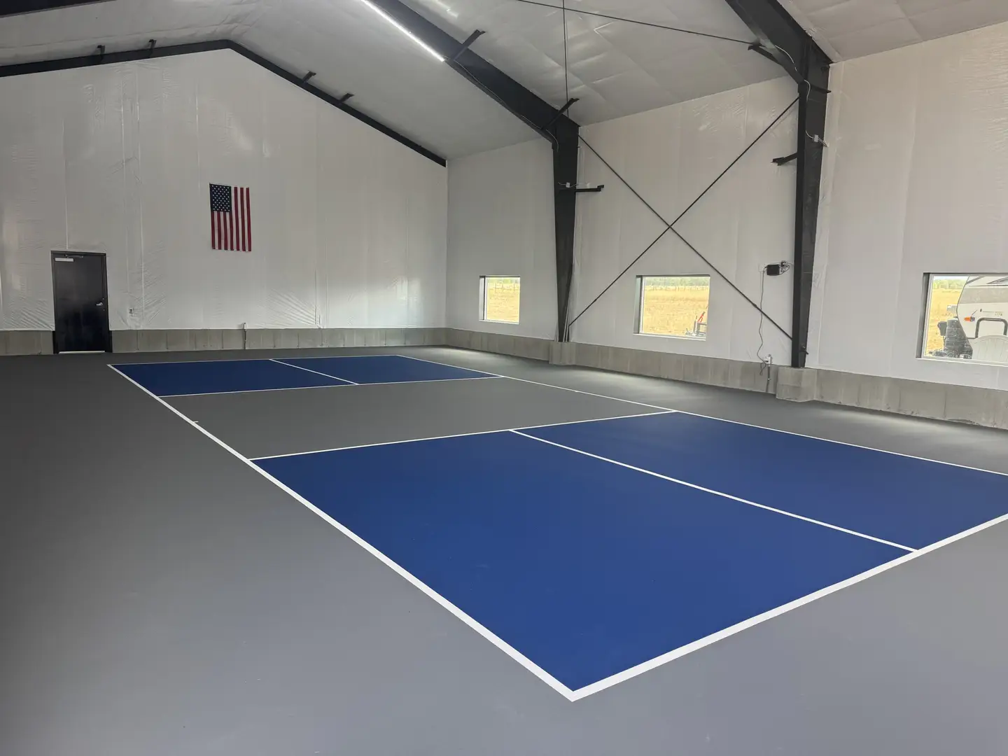 Indoor pickleball court with blue and gray surfacing and white lines.