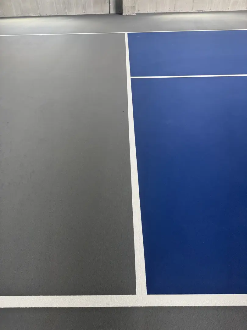 Newly painted indoor pickleball court with blue and grey surfaces.