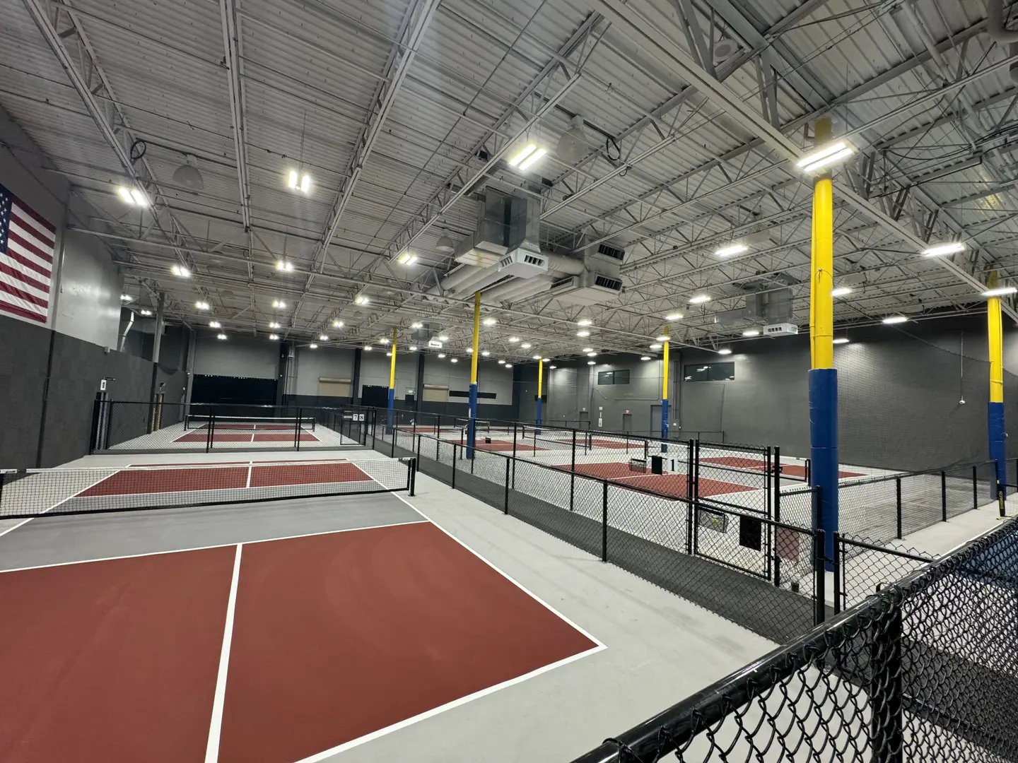 Indoor pickleball courts with red and grey surfaces, nets, and yellow support poles.