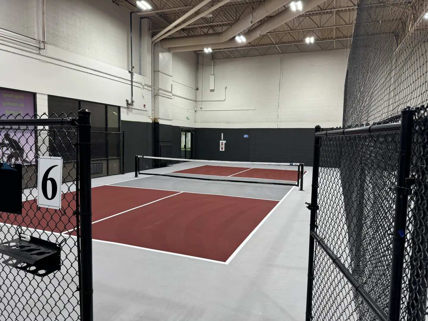 Indoor pickleball court with red and grey surface and nets.