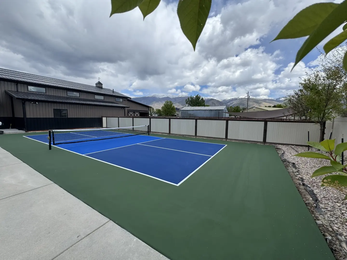 Blue pickleball court with green surround and mountains in background.