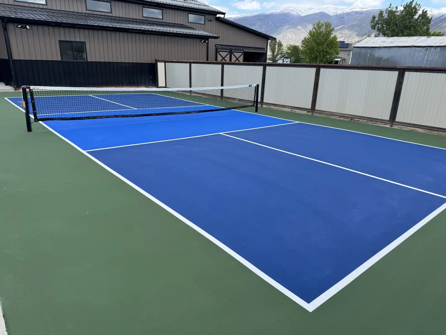 Vibrant blue pickleball court with green surround and mountain backdrop.