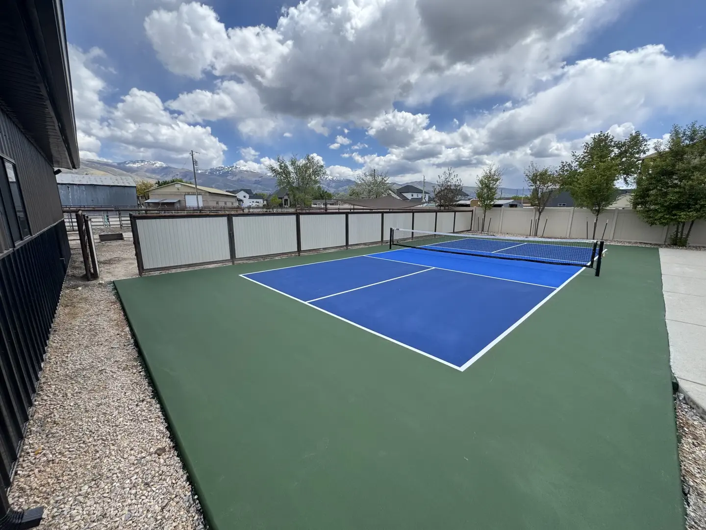 Blue pickleball court with green surround, mountains in background.