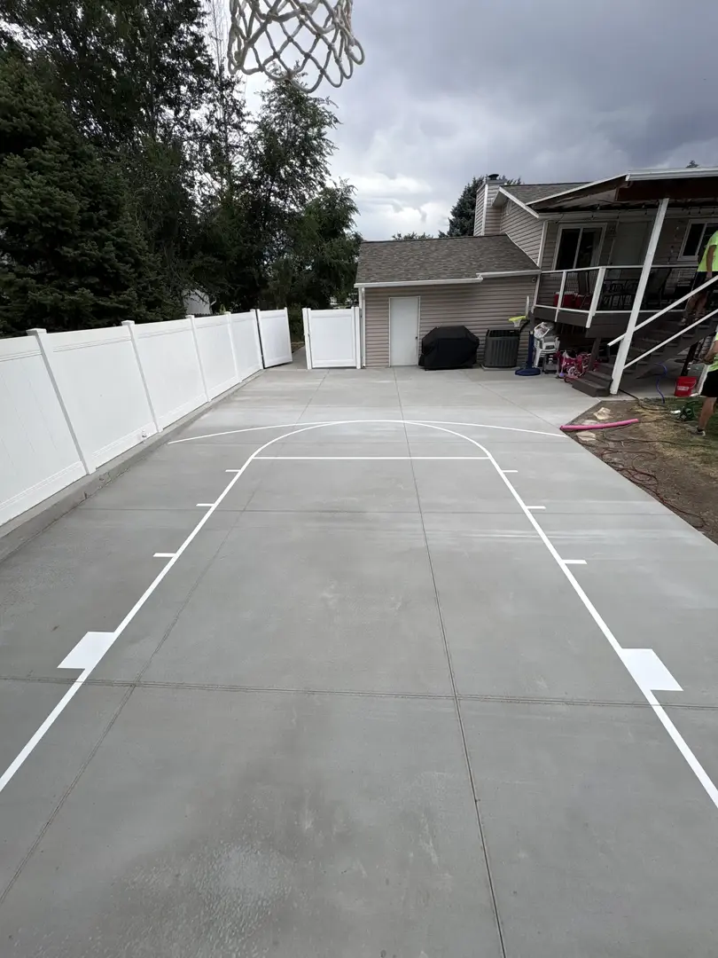 Newly painted basketball court in a backyard with white fence and house.