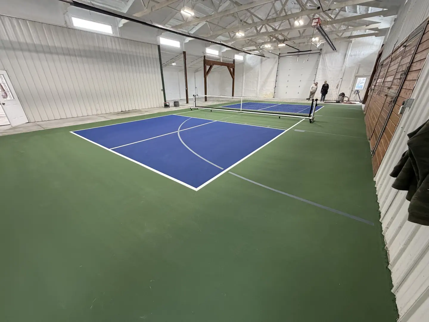 Indoor pickleball court with blue playing surface and green surround.