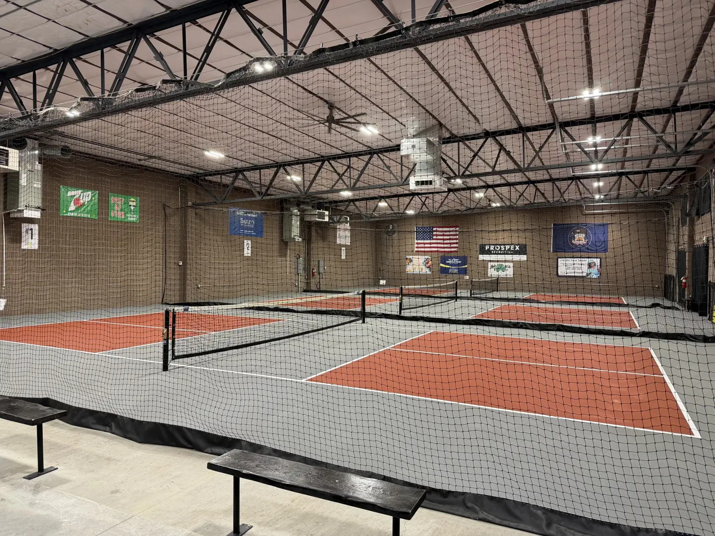 Indoor pickleball courts with orange and gray surfaces and nets.
