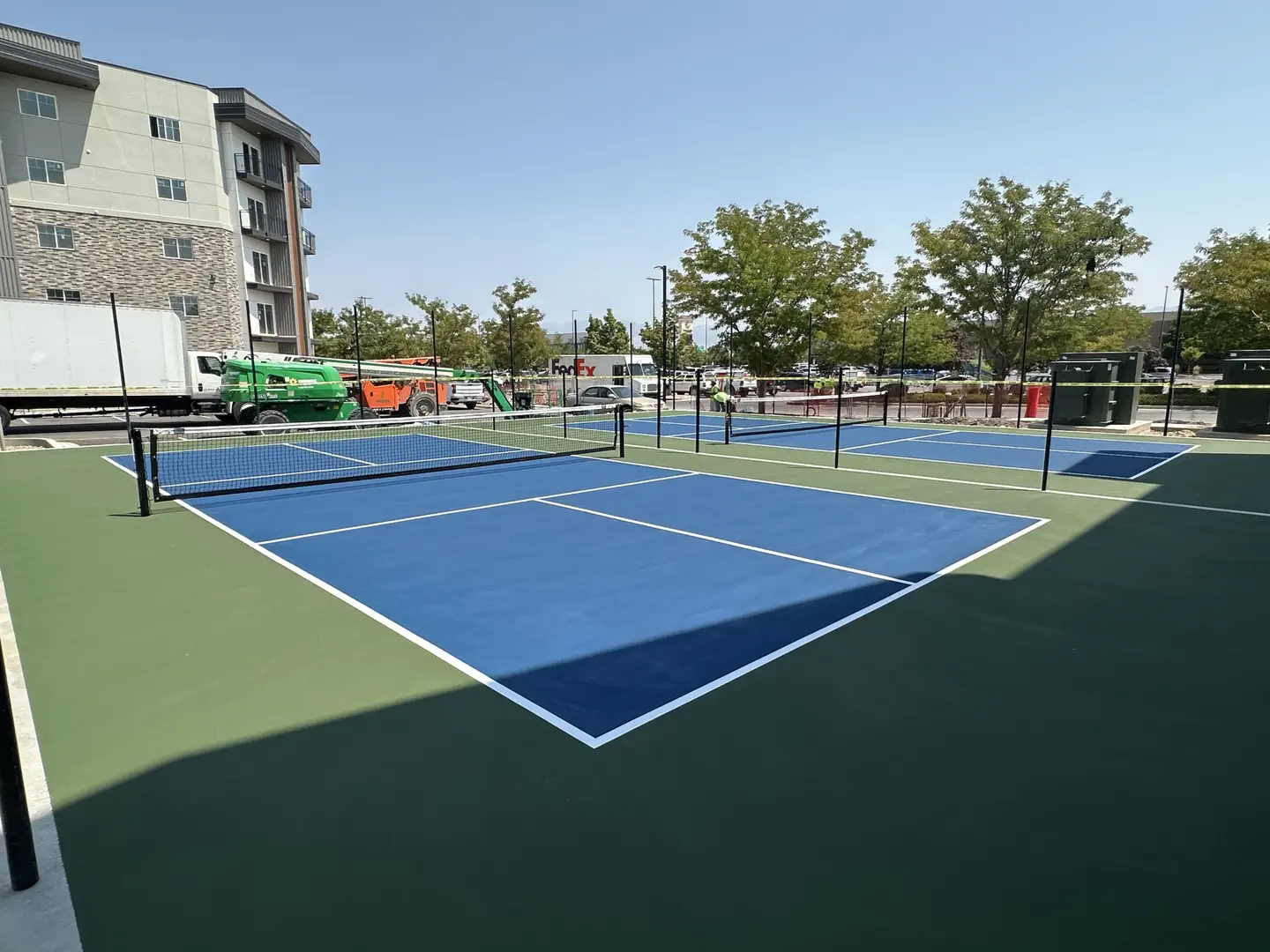 New blue pickleball courts with green surrounds and nets.