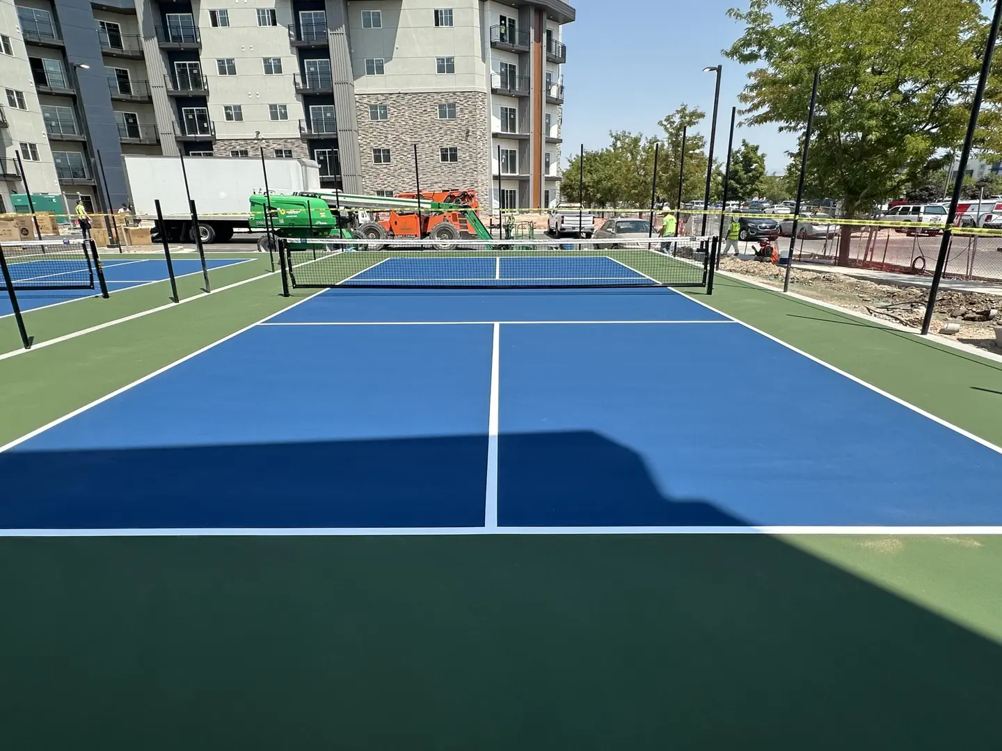 Newly constructed blue and green pickleball courts with apartment buildings in the background.