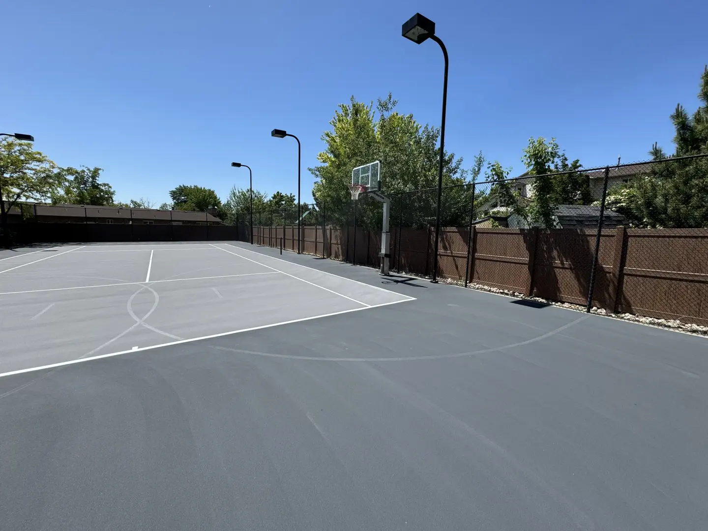 Outdoor tennis court with basketball hoop and lights