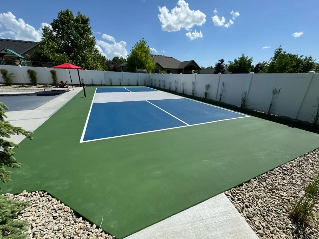 Blue and green pickleball court with white fencing and a red umbrella.