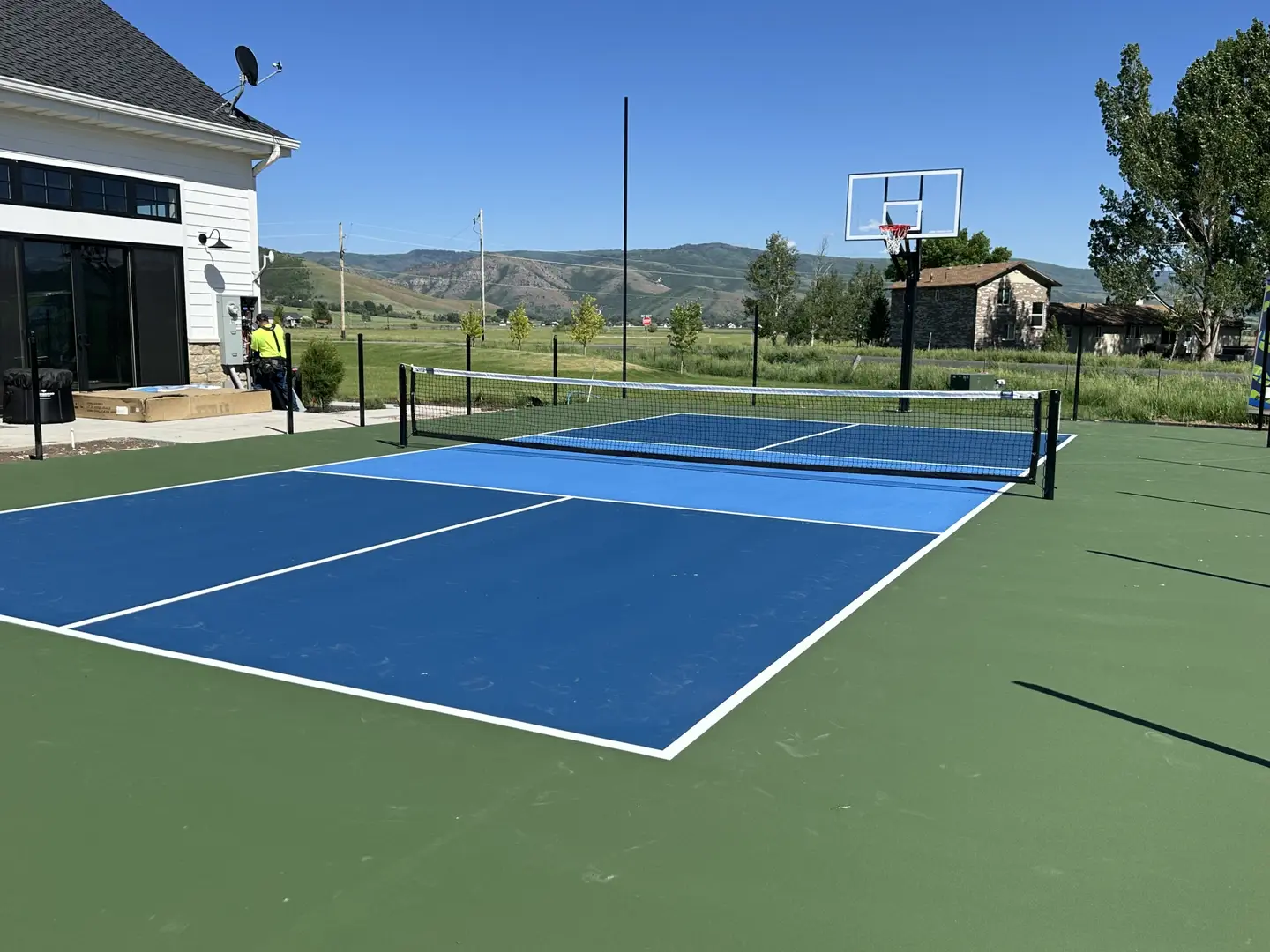 Newly installed blue pickleball court with basketball hoop in a scenic outdoor setting.