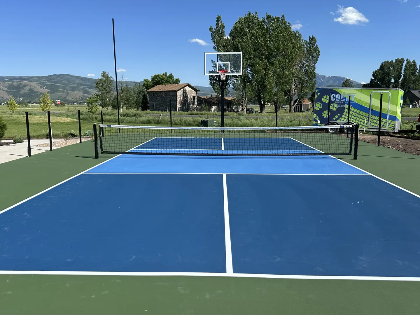 Blue and green pickleball court with basketball hoop and mountains in background