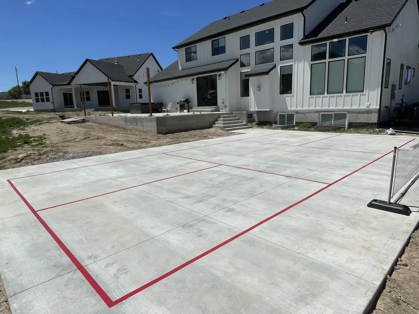 Newly painted pickleball court lines on a concrete patio next to a modern home.