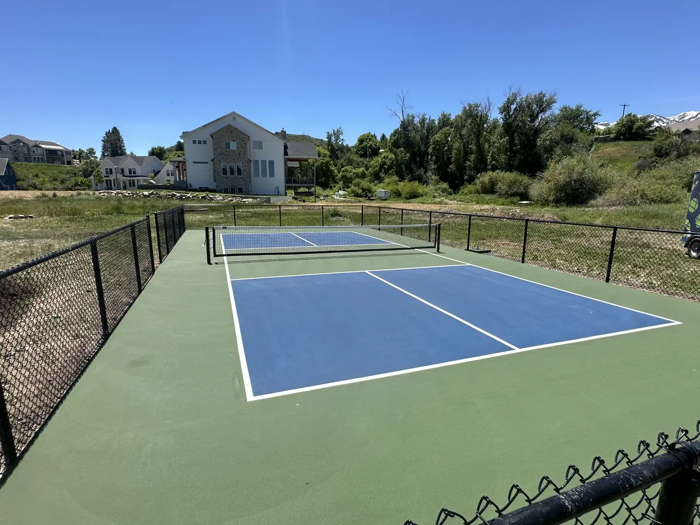 Outdoor pickleball courts with blue playing surface and green surround, fenced.