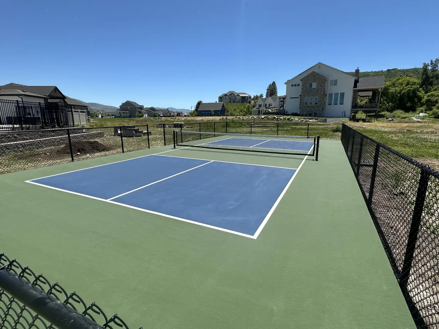 New pickleball court with blue playing surface and green surround, fenced.