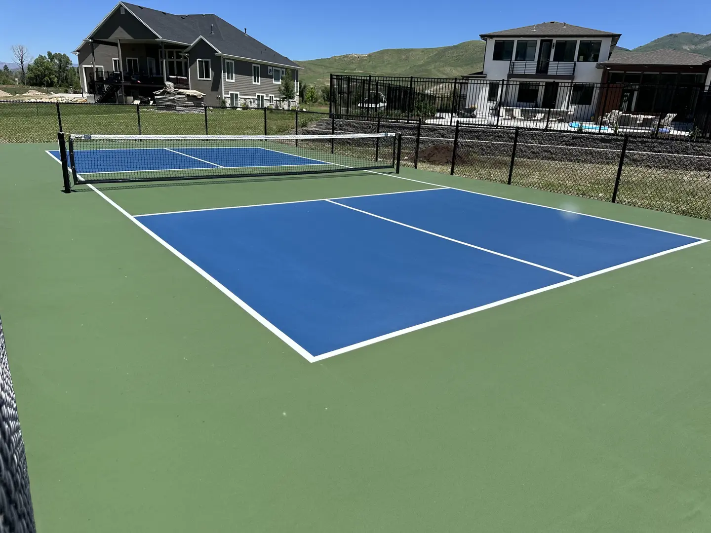 Blue pickleball court with green surround and houses in background