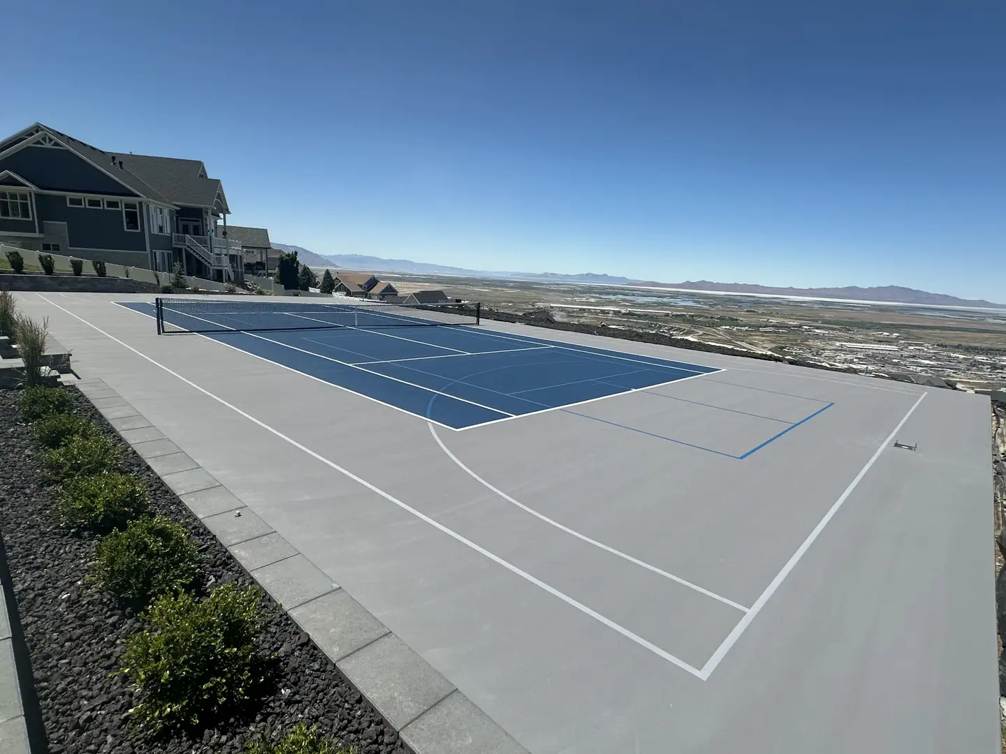 Blue tennis court with a scenic view of mountains and a valley.