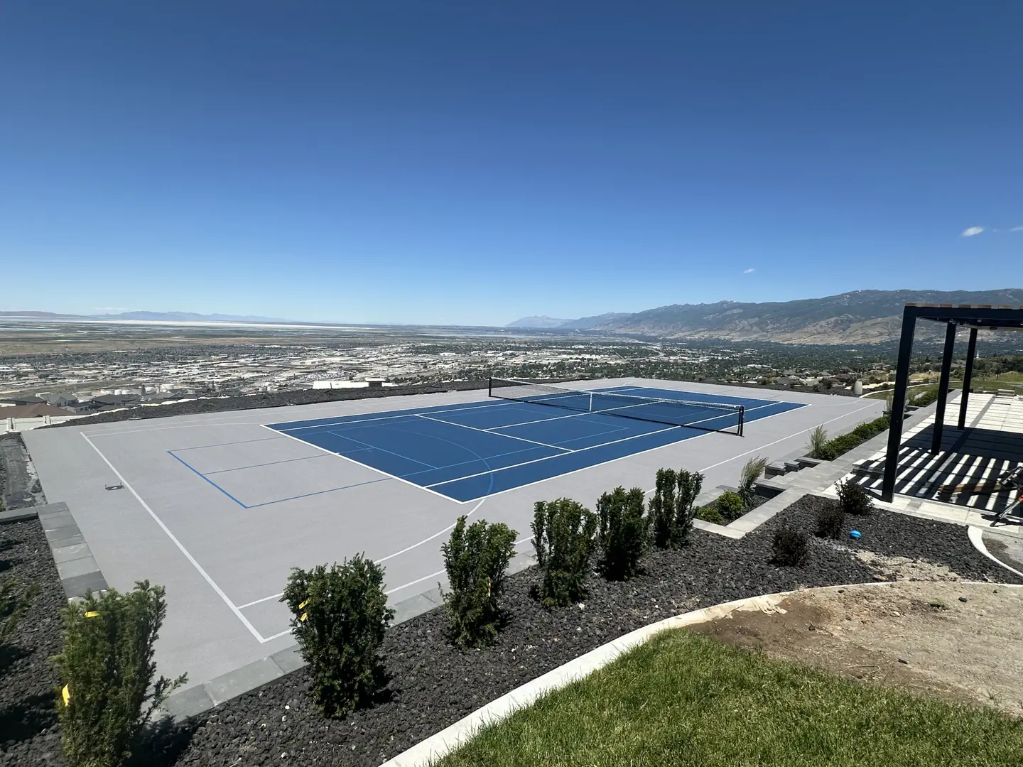 Blue tennis court overlooking a city and mountains