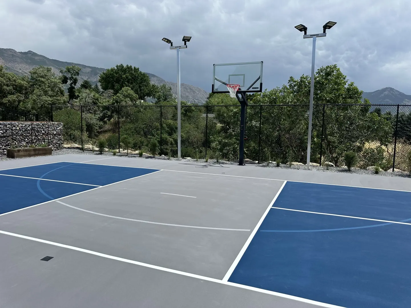Modern outdoor basketball court with blue and gray surfacing and mountain backdrop.