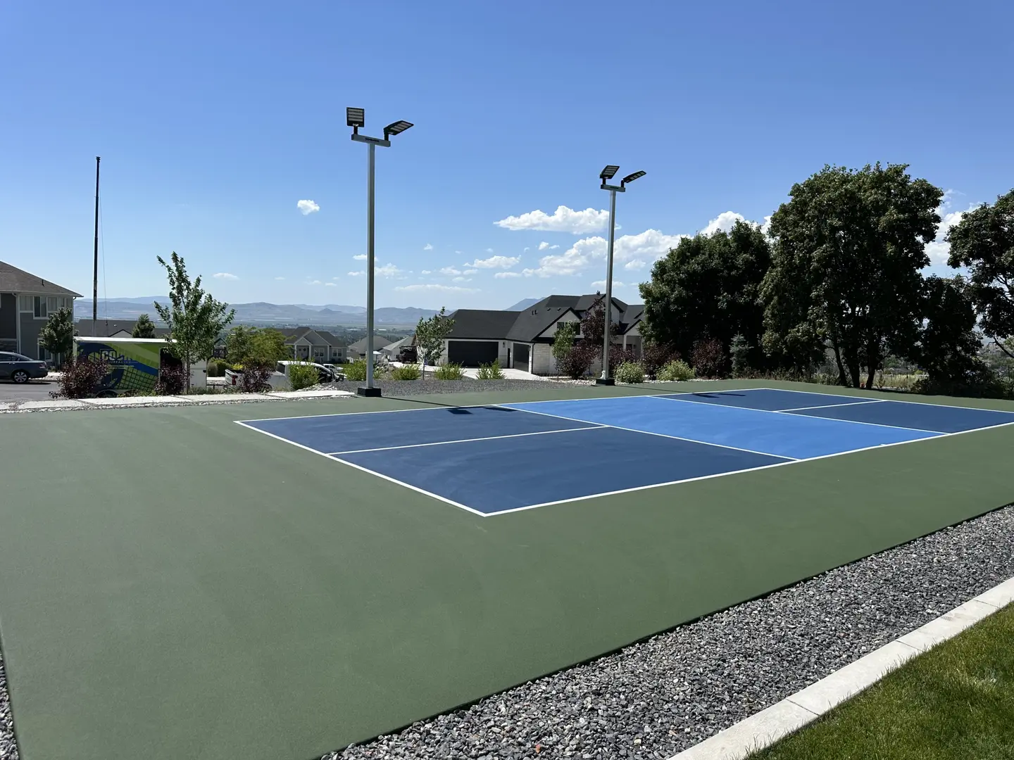 Outdoor pickleball court with blue and green surfacing and lights.