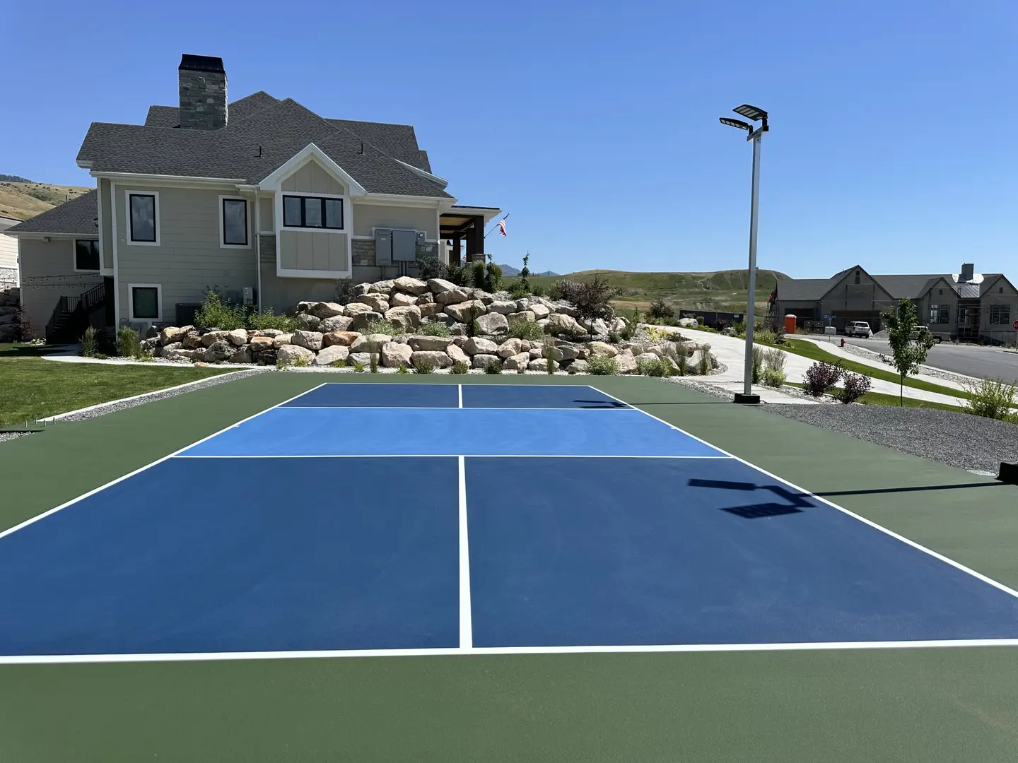 Blue and green pickleball court with a modern house and landscaped yard.