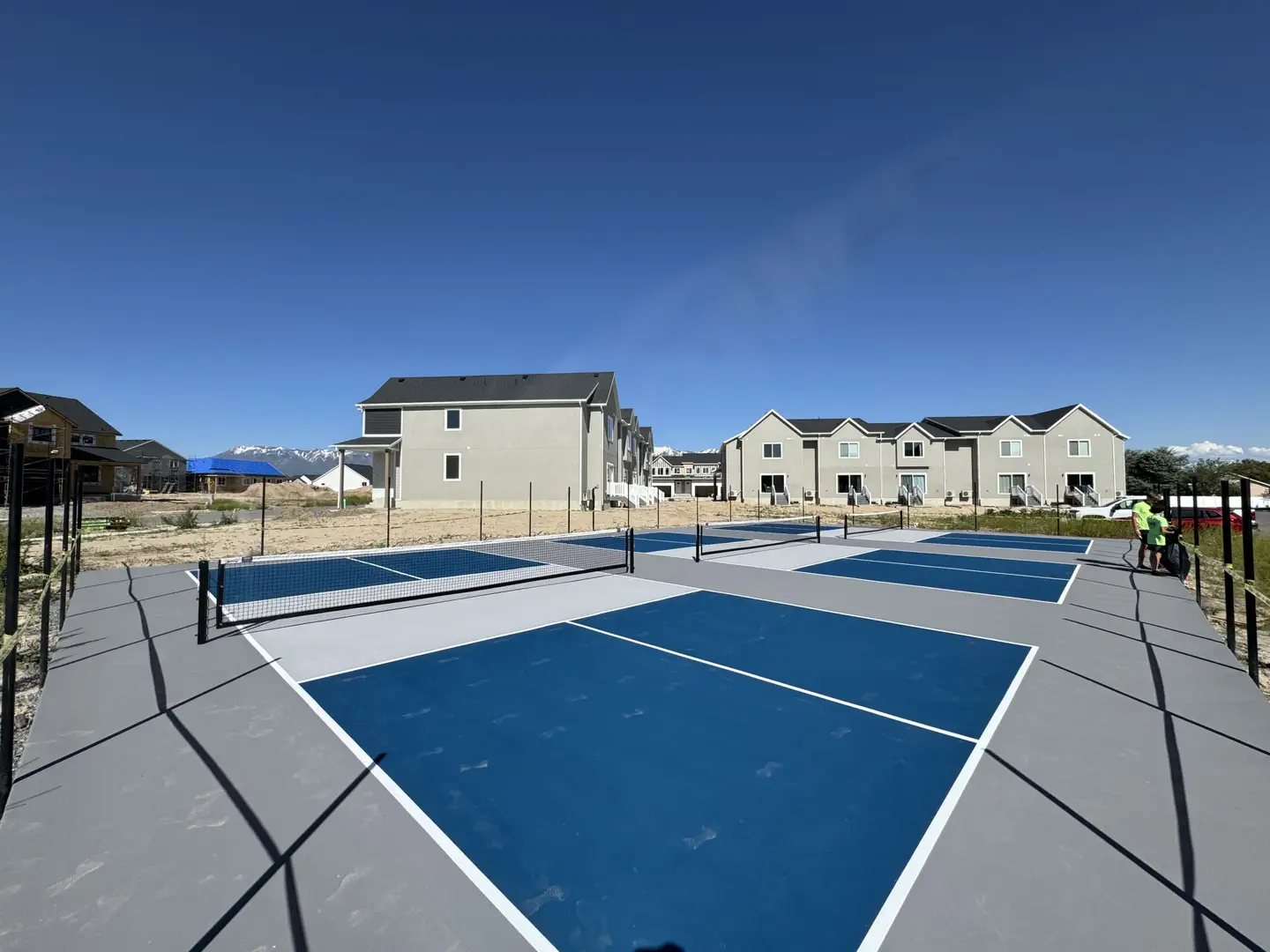 New pickleball courts with blue and gray surfaces under a clear blue sky.