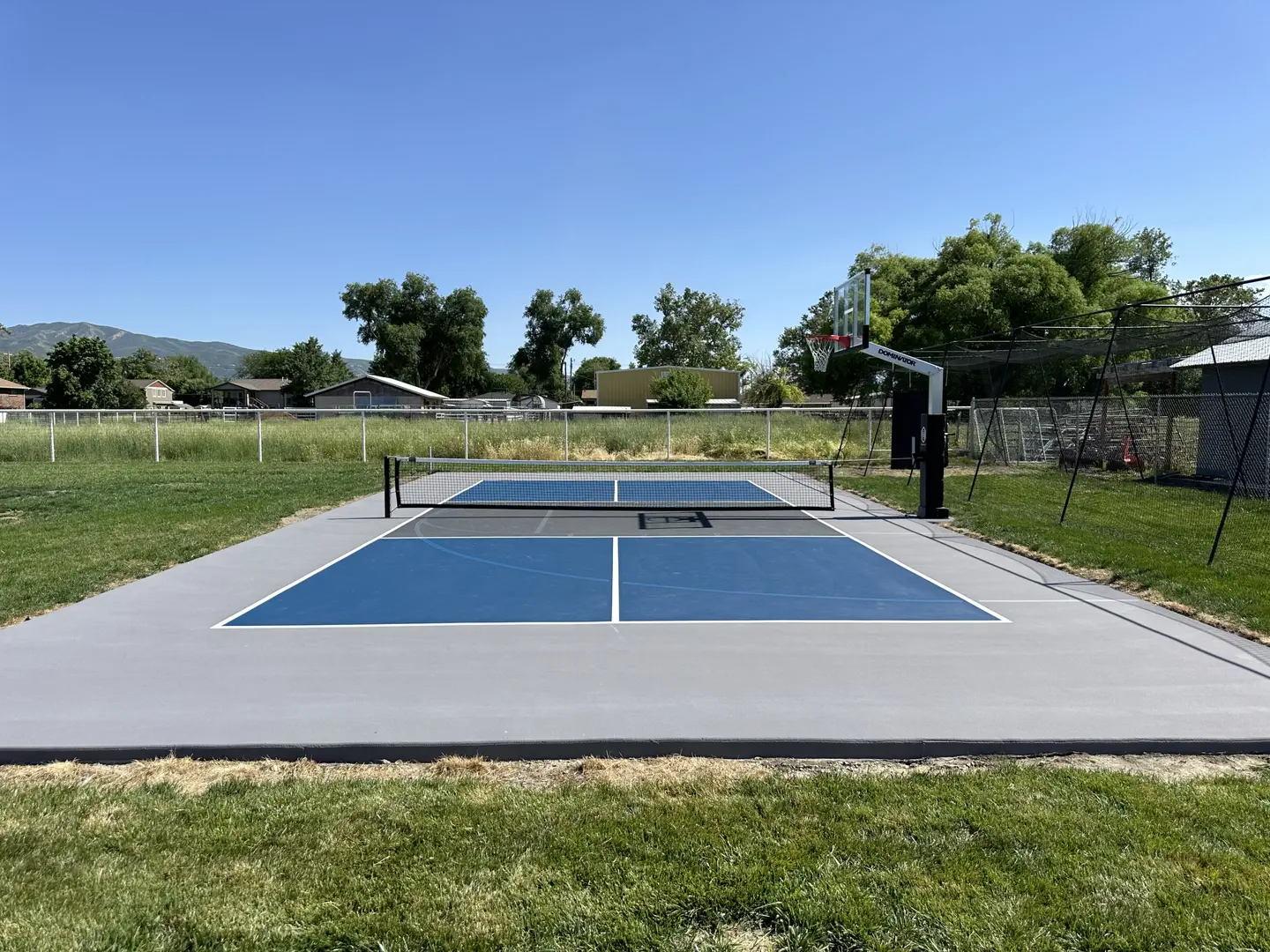 Outdoor pickleball court with a basketball hoop in a residential backyard.