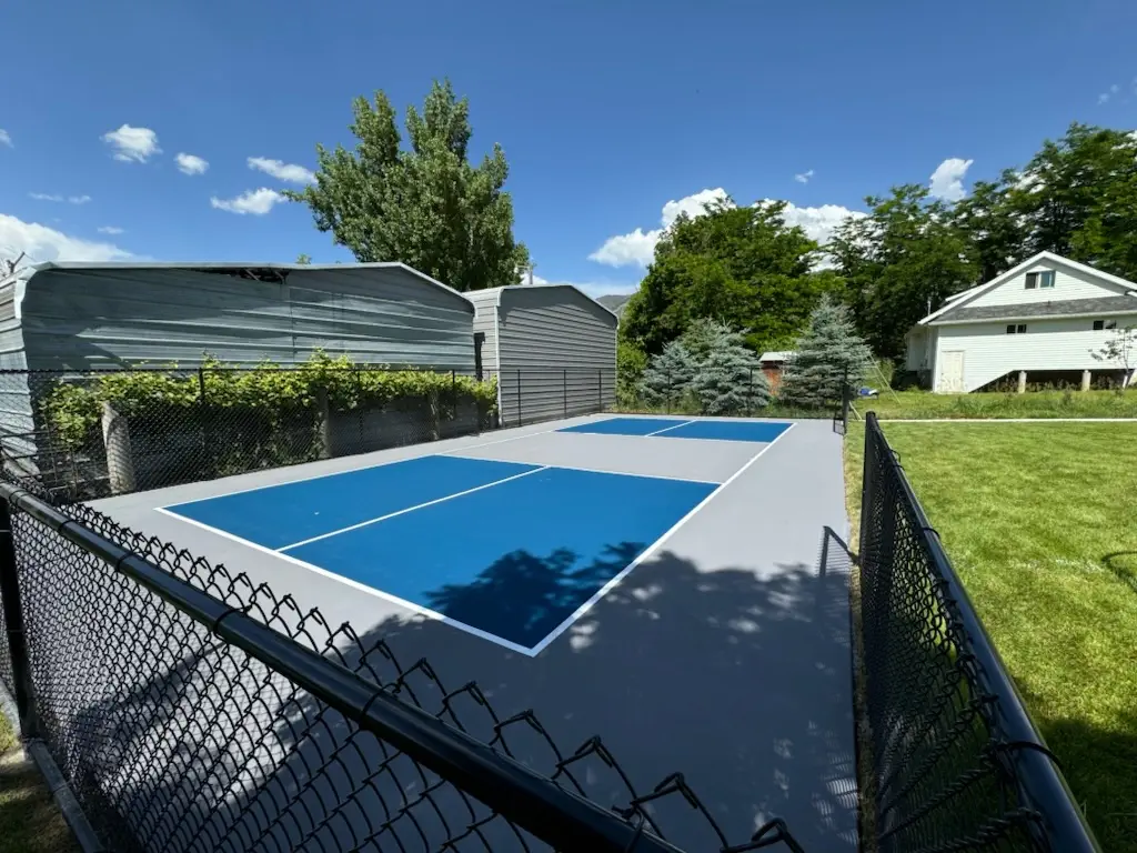 New blue and gray pickleball court in a backyard with a fence.