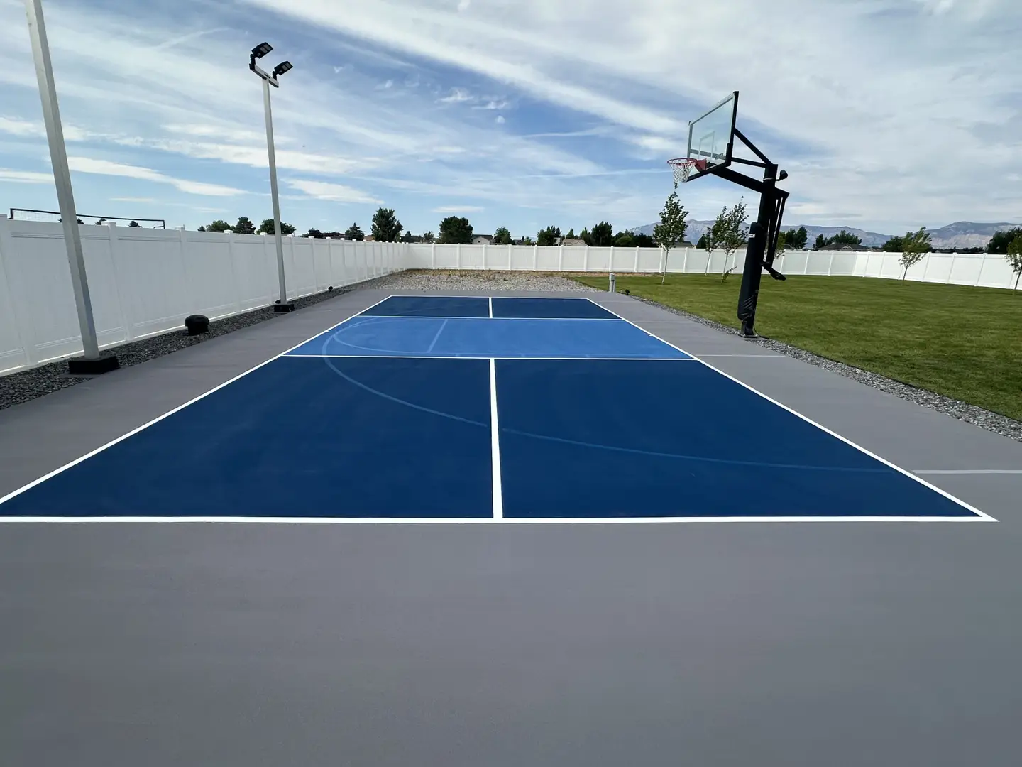 Outdoor basketball court with blue and grey surfacing and a basketball hoop.