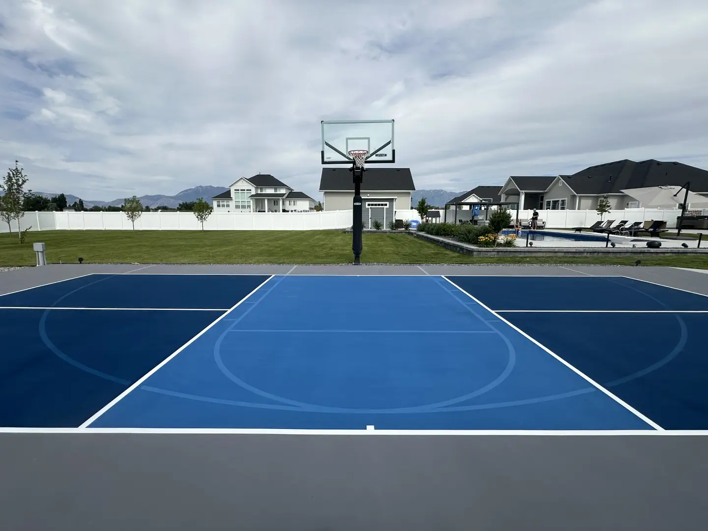 Modern backyard basketball court with blue and gray surfaces.