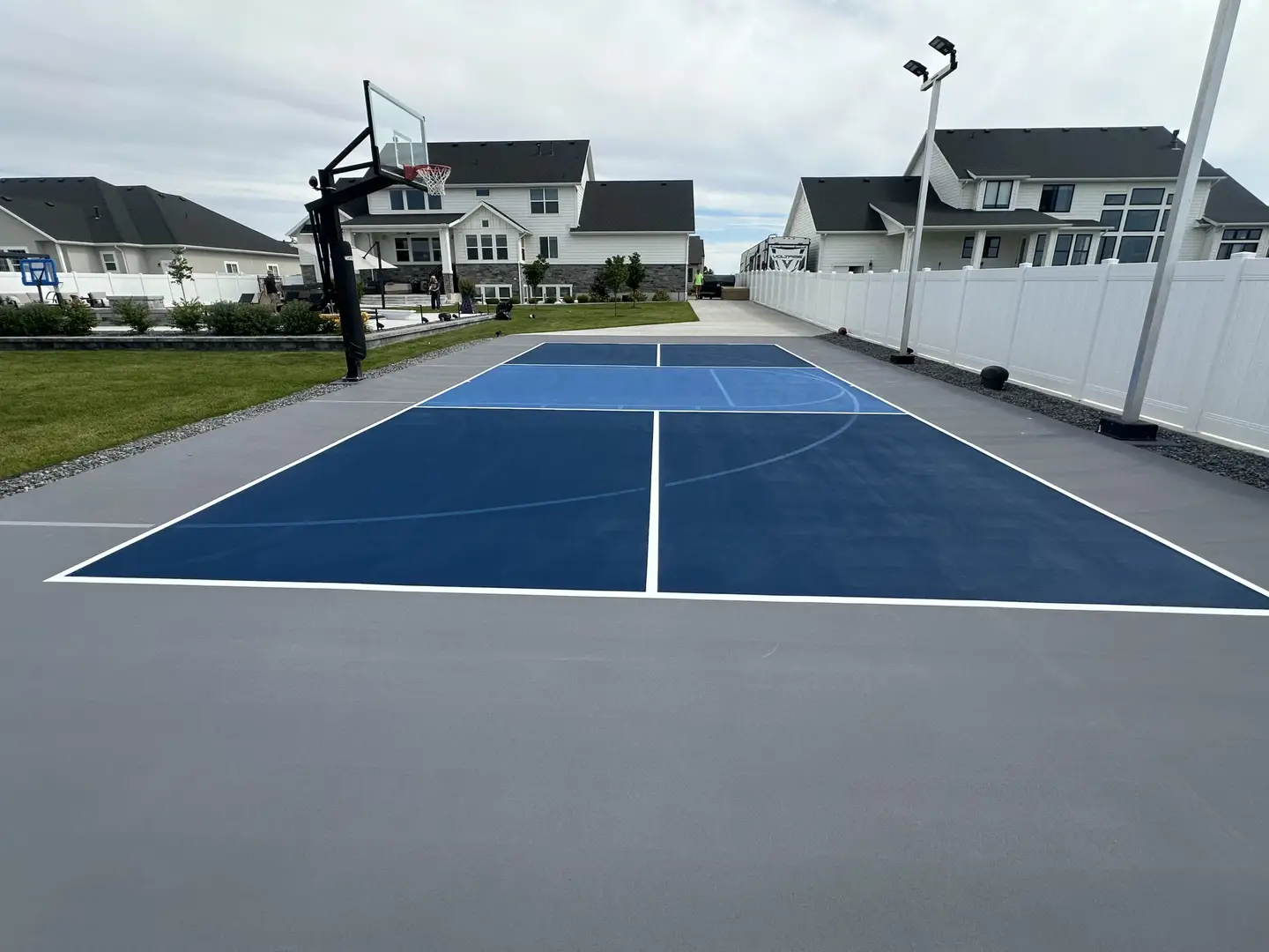 Modern backyard basketball court with blue and grey surfacing.